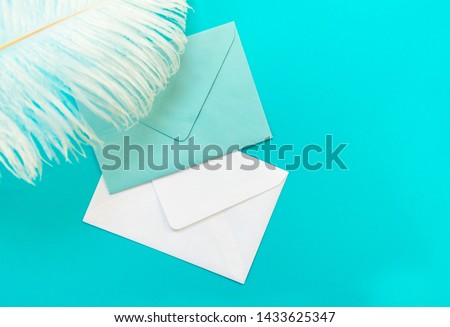 Two blue and white envelopes and a feather isolated against a blue background. Greeting card concept. Copy space.