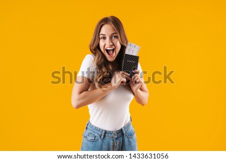 Photo of charming young woman rejoicing while holding passport and travel tickets isolated over yellow background