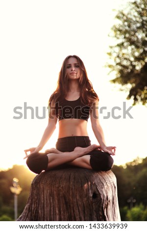 Young caucasian woman practicing yoga on a stump in the park