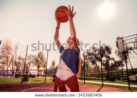 Pleasant summer season. Active young female player rising hands with ball while entertaining herself with sportive exercises