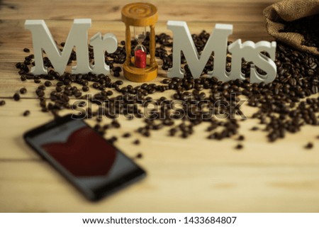 Mr and Mrs word text wedding sign with hourglass and red heart picture in smart phone on bright wooden background surroundig brown roasted coffee beans.