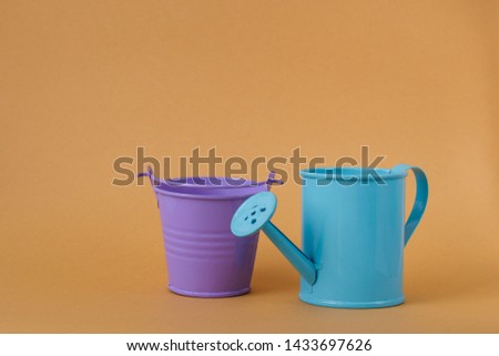 Toy iron blue watering can and purple bucket on an orange background. Place for text. Agriculture concept.