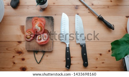 Still life picture of santoku knife with tomato on wooden table.