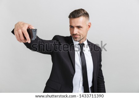 Image of successful handsome businessman in formal suit taking selfie photo on cellphone isolated over gray background