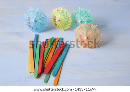 Accessories for cocktails and ice cream, umbrella, wooden colored chopsticks-spoons on a blue wooden background. Decoration of drink and ice cream.