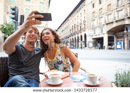 Portrait of beautiful ethnic diverse young tourist couple joyful in coffee shop on vacation using smartphone to take selfies photos, networking outdoors. Travel holiday leisure recreation lifestyle.