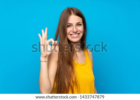 Young woman with long hair over isolated blue wall showing ok sign with fingers