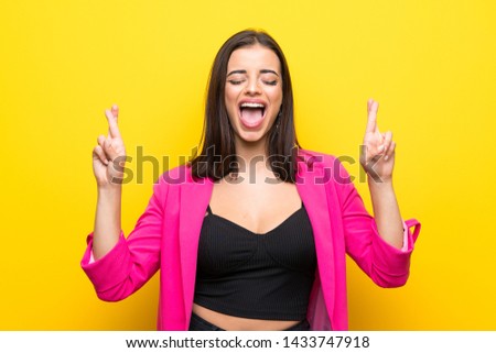 Young woman over isolated yellow background with fingers crossing