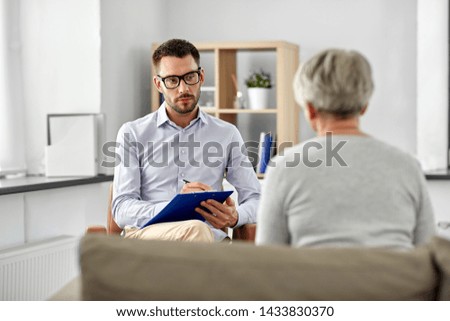 geriatric psychology, mental therapy and old age concept - psychologist with clipboard taking notes and listening to senior woman patient at psychotherapy session Royalty-Free Stock Photo #1433830370