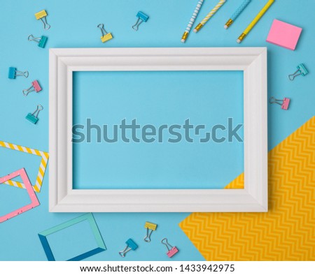 Flat lay empty frame and office supplies on blue pastel background with copy space. 