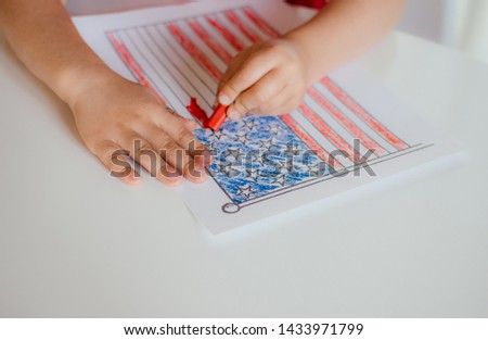 The child's hands paints the American flag on white table. Children's drawing of the flag of America. Independence day, July 4.