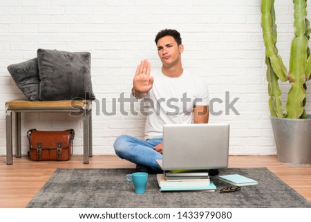 Handsome man sitting on the floor with his laptop making stop gesture with her hand