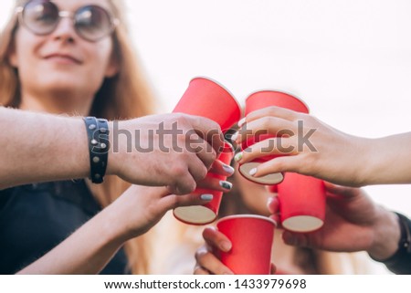 group of happy friends relaxing on nature with red cups of alcohol. celebration, friendship group of smiling friends toasting non alcoholic drinks. red cardboard cup. close-up portrait