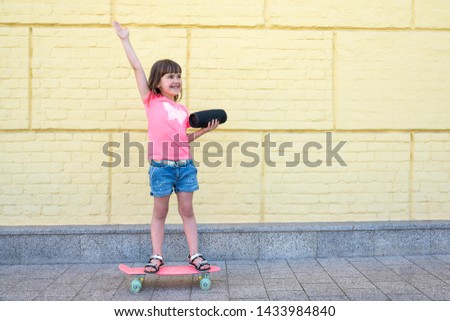 A girl is skateboarding with a music bluetooth speaker in the city at the yellow brick wall background.