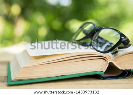 Open book and eyeglasses on a wooden table in a garden. Sunny summer day, reading in a vacation concept
