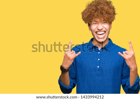 Young handsome elegant man with afro hair shouting with crazy expression doing rock symbol with hands up. Music star. Heavy concept.