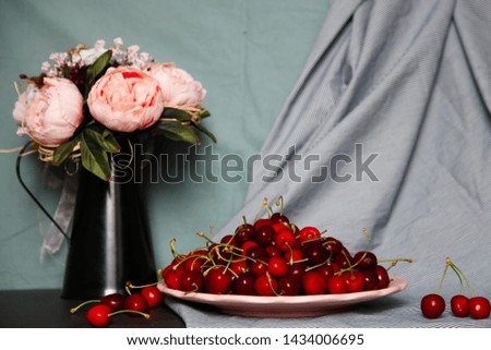 Still life of sweet cherries and flowers in an iron jug against a background of fabrics. Still life concept. 