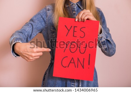 Woman holding paper with text yes you can while standing in front of the wall.