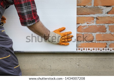 Worker placing styrofoam, polystyrene thermal insulation to brick wall, house renovation Royalty-Free Stock Photo #1434007208