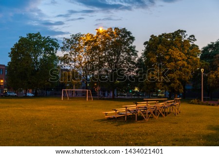 Landscape photo of a football field in a city park in the evening with bleachers and a goal lit up by a lamp post. Shot in Montreal, Quebec, Canada. 