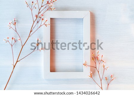 White wooden frame on a white textured background with small flowers - a template for a greeting card or invitation