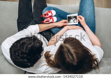 A man, husband hugging his pregnant wife in the home. Happy family pregnancy. Young expecting woman holds baby. waiting for a miracle.first picture of an ultrasound in the hands of parents