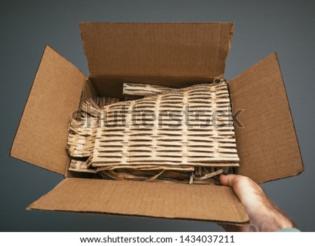 Man hand holding open cardboard box after before unboxing with protective paper carton