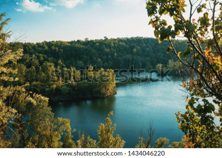 Scenery blue autumn pond with green leaf forest on background. Blue deep sky. Ukrainian nature 