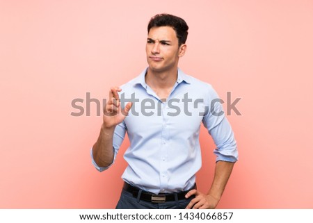 Handsome man over pink background with fingers crossing and wishing the best