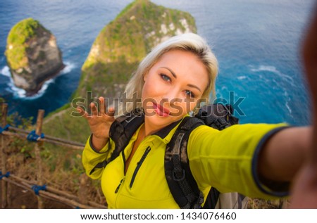 outdoors lifestyle portrait of young beautiful and happy hiker woman with backpack hiking on sea mountain cliff taking selfie portrait with mobile phone enjoying solo travel trekking adventure