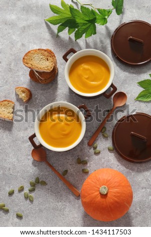 Healthy pumpkin cream soup in casserole bowls with autumn decoratin 