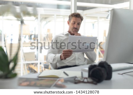 Front view of thoughtful Caucasian male graphic designer looking at photograph on desk in a modern office