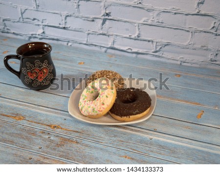 A ceramic cup with tea and a white porcelain plate with donuts in the icing.