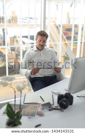 Front view of Caucasian male graphic designer looking at photograph on desk in a modern office