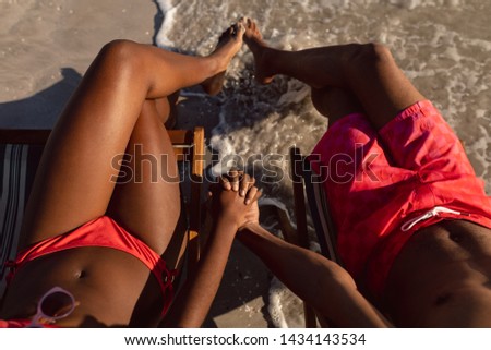 Low section of African-american couple relaxing with hand in hand on the beach Royalty-Free Stock Photo #1434143534