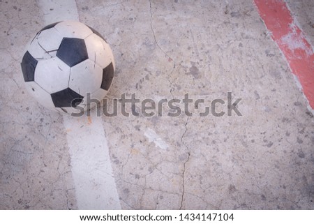 Old ruined damaged soccer ball put on white line  in cracked cement field with sun light. What is broken, nobody is interested. Copy space and concept image.