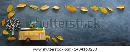 education and back to school concept. Top view photo of cardboard bus and pencils next to tree with autumn dry leaves over classroom blackboard background