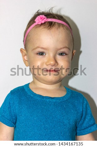 Very cute 20 months old baby portrait. Beautiful 1 year old toddler girl, posing naturally. Little girl, wearing cute blue dress and a pink headband.  Studio head shot, green eyes are visible, smiling