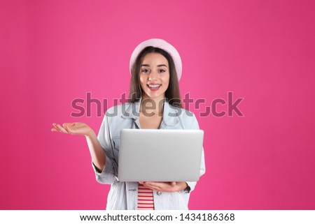 Portrait of young woman in casual outfit with laptop on color background