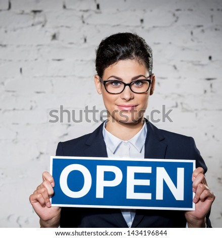 Portrait of beautiful young businesswoman holding open sign placard against brick wall