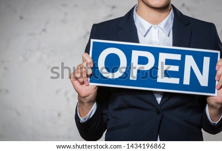 Midsection of young businesswoman holding open sign placard against brick wall