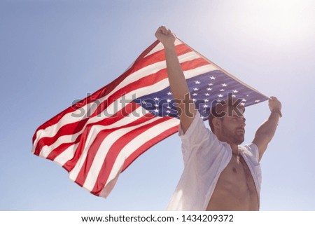 Low angle view of young Caucasian man waving american flag on beach in the sunshine