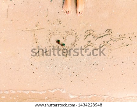 Inscription on wet sand I love sea with symbols with woman feet. Holidays by the sea. Travel concept