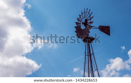 A tall windmill in a farm standing in front of a beautiful blue sky