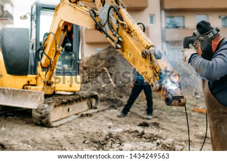 Construction worker welding broken excavator on construction site