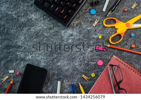 Multicolored school supplies on black and yellow blackboard background ready for your design with copy space. Stationery objects and gadgets for the modern student. Back to school concept.