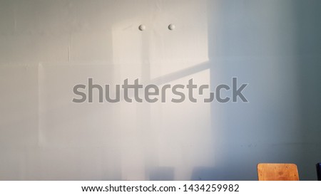 Old white plastering wall surface with blurry geometric shadows and top of wooden chair in corner. Cross shaped shadows with two round dots. Crossed lines shadow background. Light and shadow backdrop.