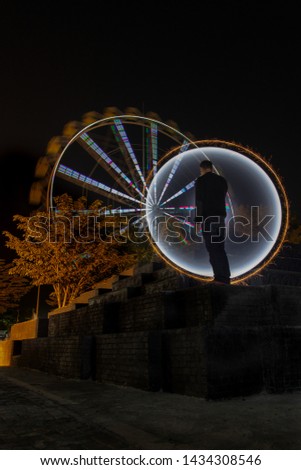 a man wearing a black jacket was standing alone decorated with a yellow circle light painting as a backdrop on the site area of ​​a night tour
