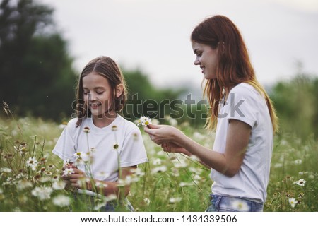 The girl and mother gathers flowers on a meadow cropped view of green grass