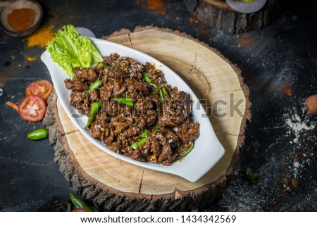 Stock Photo of Crispy shredded beef with chilli and sweet chilli sauce on white dish placed on wooden log. Chinese takeaway food